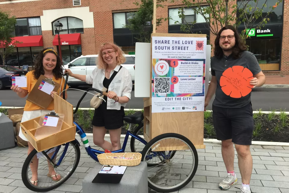 A group of people gather around an information booth to share ideas about the future of South Street in Philadelphia.